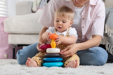Photo of Mother and her little baby playing with toy pyramid on floor at home, closeup