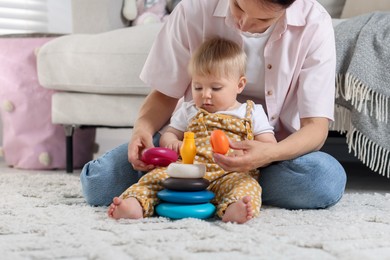 Photo of Mother and her little baby playing with toy pyramid on floor at home