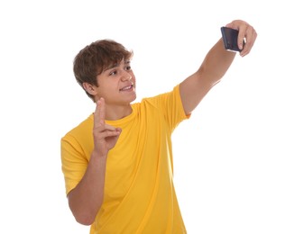 Photo of Smiling teenage boy taking selfie by smartphone and showing peace sign on white background