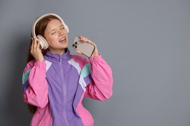 Photo of Happy teenage girl in headphones with smartphone singing on grey background. Space for text