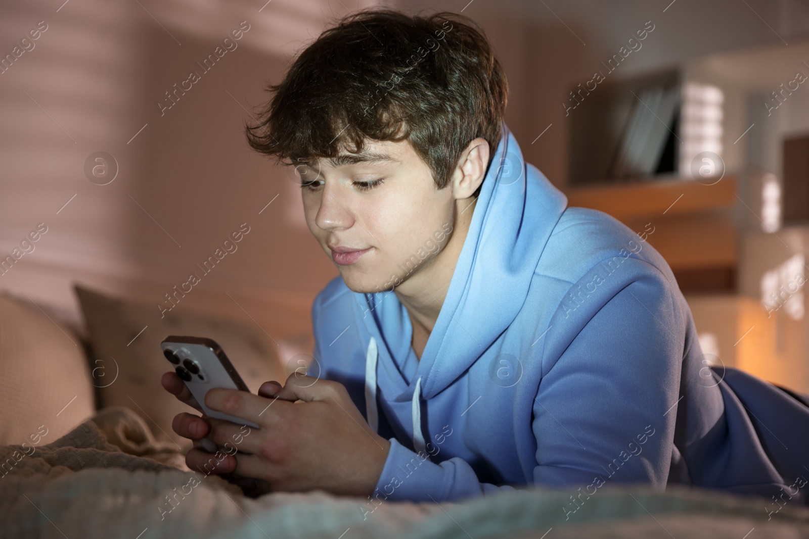 Teenage boy using smartphone on bed at home Photo of Teenage boy using smartphone on bed at home