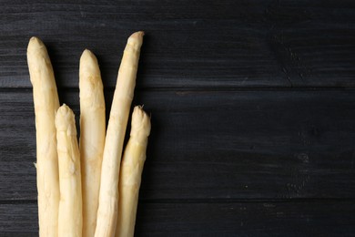 Photo of Raw white asparagus spears on black wooden table, flat lay. Space for text