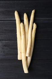 Photo of Raw white asparagus spears on black wooden table, top view