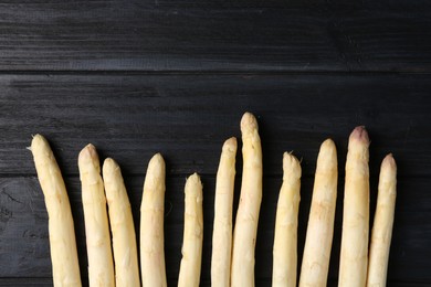 Photo of Raw white asparagus spears on black wooden table, flat lay. Space for text