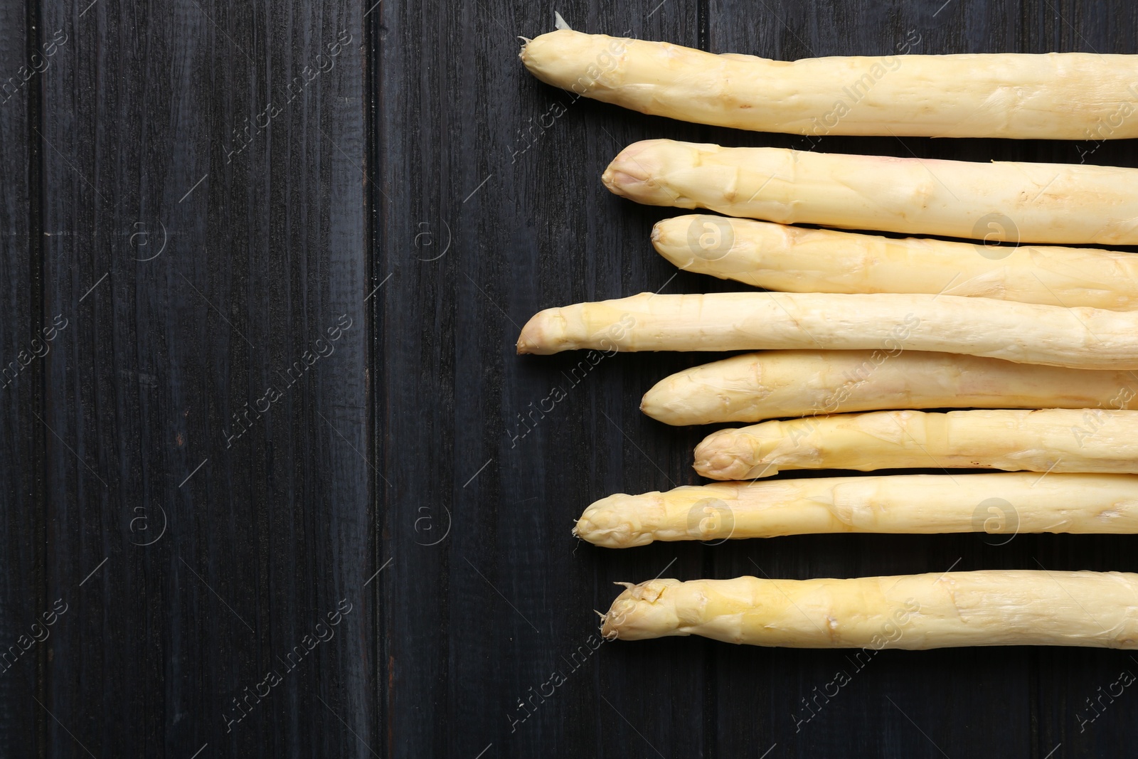 Raw white asparagus spears on black wooden table, flat lay. Space for text Photo of Raw white asparagus spears on black wooden table, flat lay. Space for text