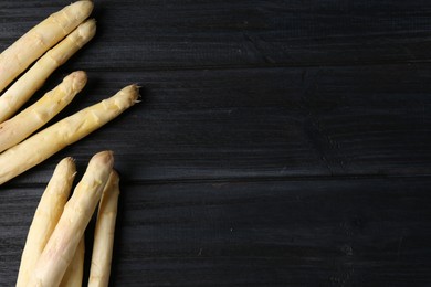 Photo of Raw white asparagus spears on black wooden table, flat lay. Space for text
