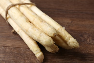 Photo of Bunch of raw white asparagus spears on wooden table, closeup
