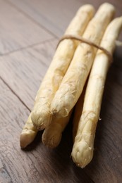 Photo of Bunch of raw white asparagus spears on wooden table, closeup