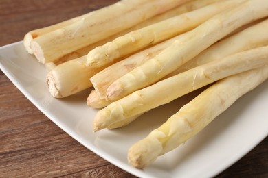 Photo of Raw white asparagus spears on wooden table, closeup