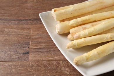 Photo of Raw white asparagus spears on wooden table, closeup. Space for text