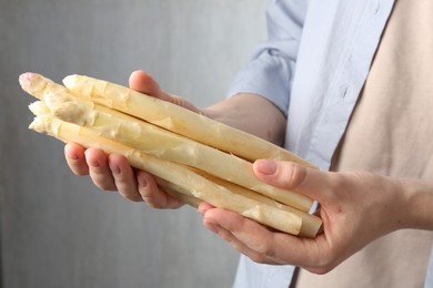 Photo of Woman with raw white asparagus spears on grey background, closeup