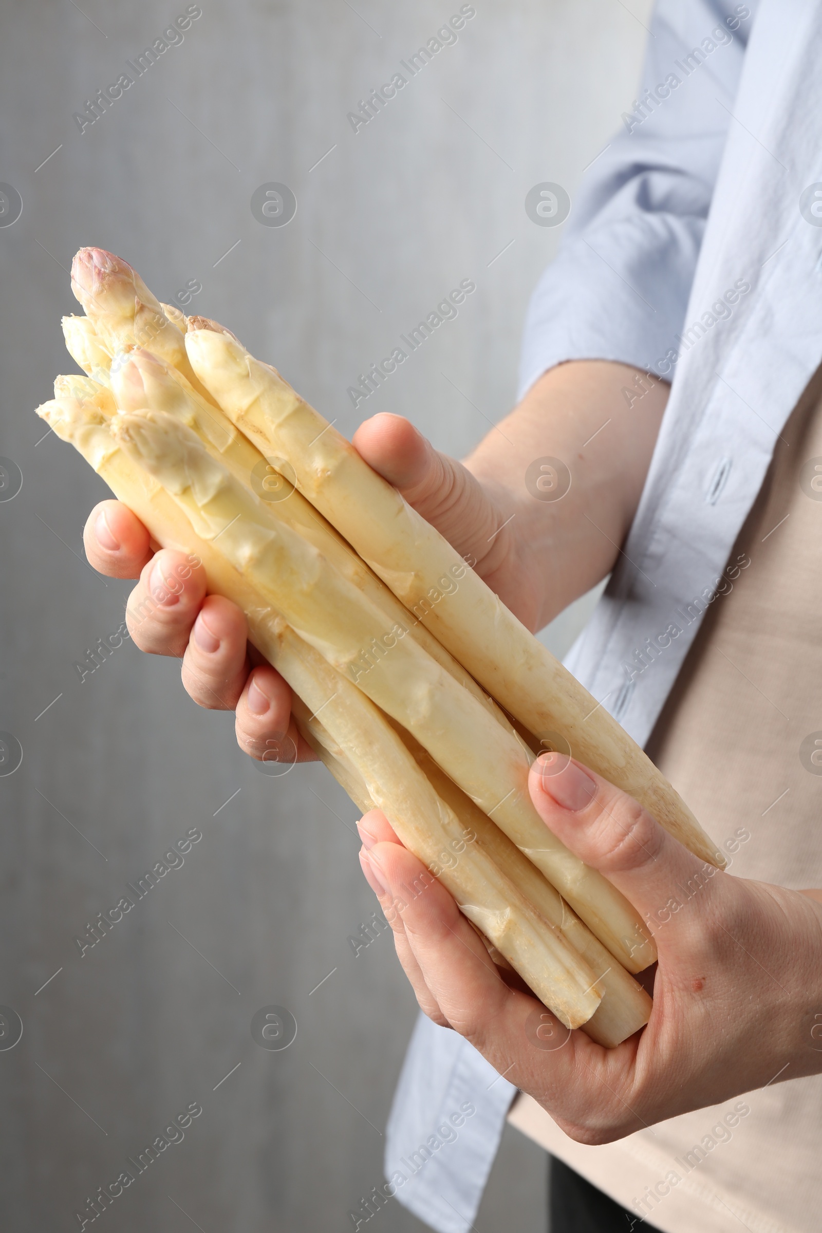 Woman with raw white asparagus spears on grey background, closeup Photo of Woman with raw white asparagus spears on grey background, closeup