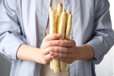 Photo of Woman with raw white asparagus spears on grey background, closeup