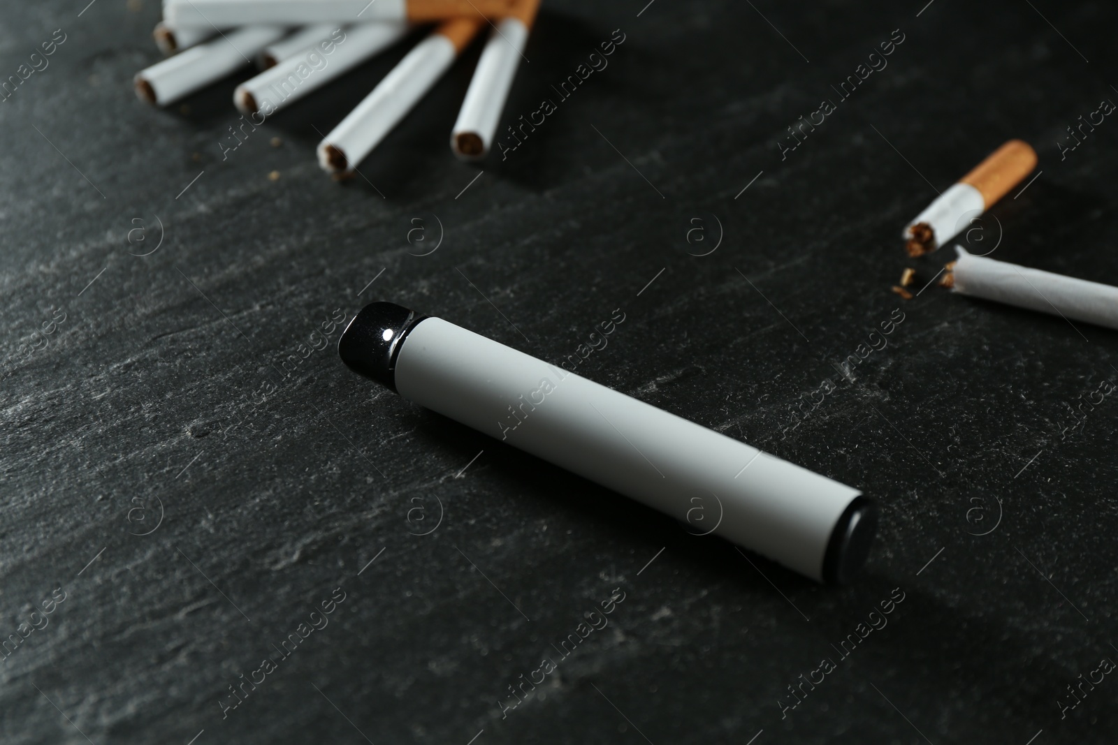 Photo of Electronic smoking device and cigarettes on black table, closeup