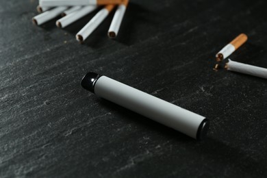 Photo of Electronic smoking device and cigarettes on black table, closeup