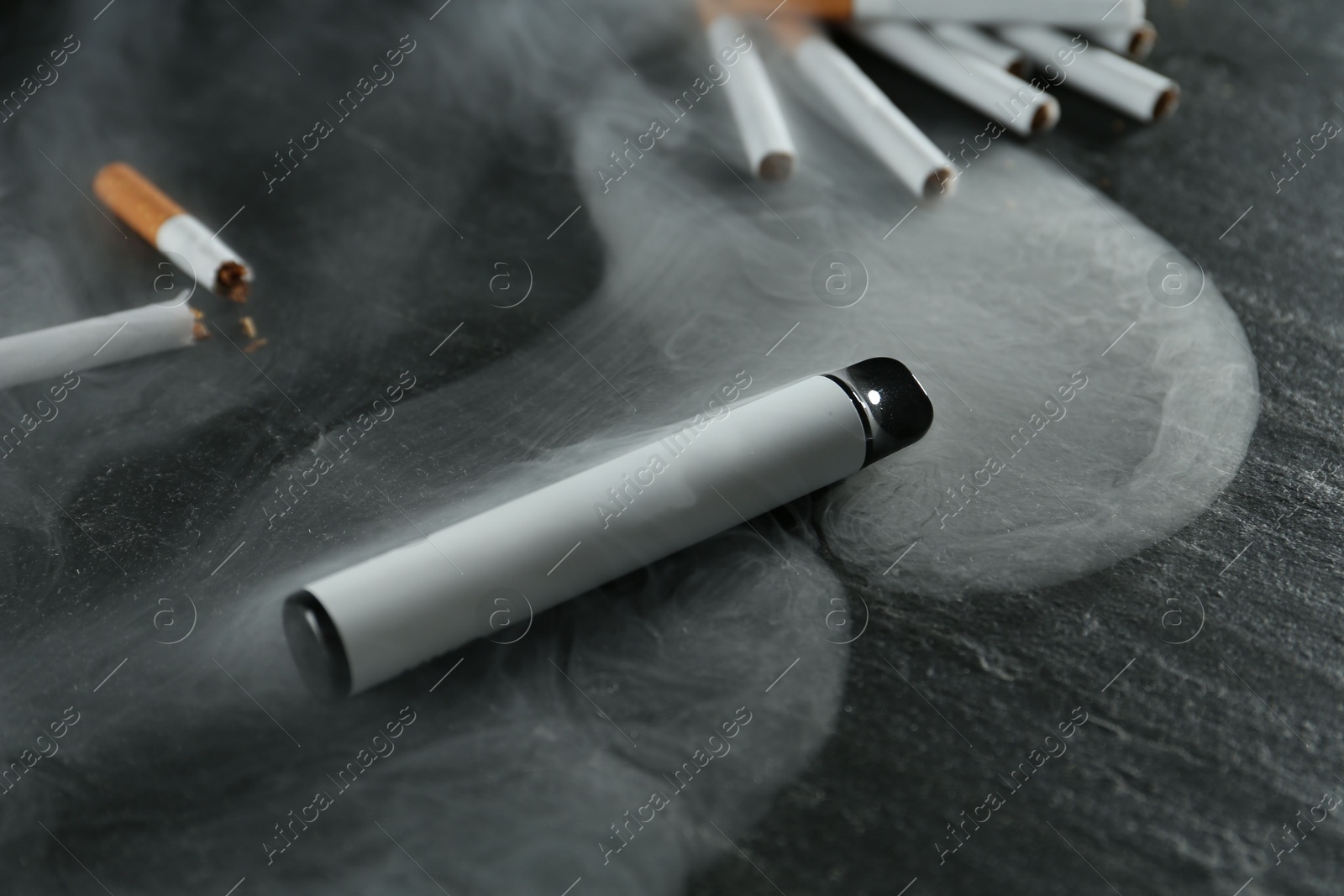 Photo of Electronic smoking device and cigarettes on black table, closeup