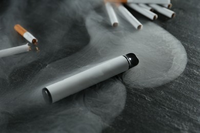 Photo of Electronic smoking device and cigarettes on black table, closeup