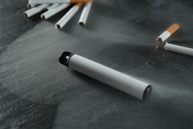 Photo of Electronic smoking device and cigarettes on black table, closeup