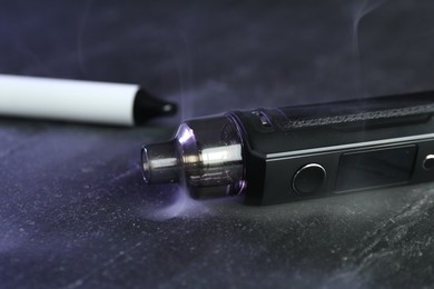 Photo of Modern electronic smoking devices on black table, closeup