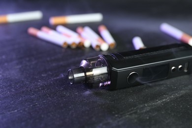 Photo of Electronic smoking device and cigarettes on black table, closeup