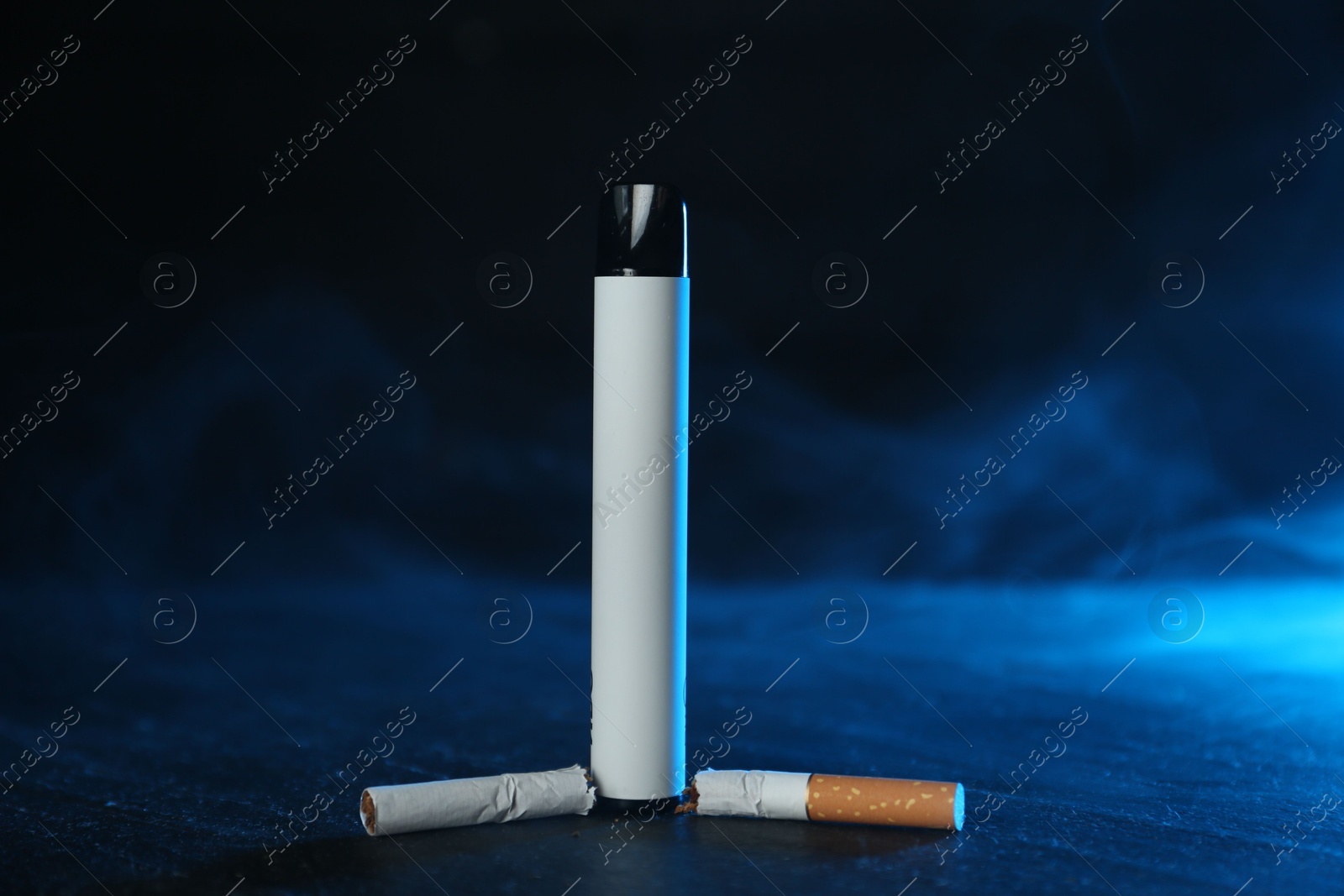 Electronic smoking device and broken cigarette on black table in blue light Photo of Electronic smoking device and broken cigarette on black table in blue light