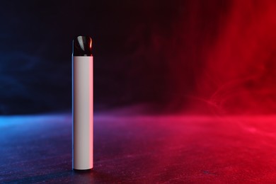 Photo of Electronic smoking device on black table in red light. Space for text
