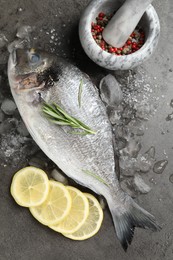 Photo of Fresh raw dourade fish, ice, lemon slices and rosemary on grey table, flat lay. Organic seafood