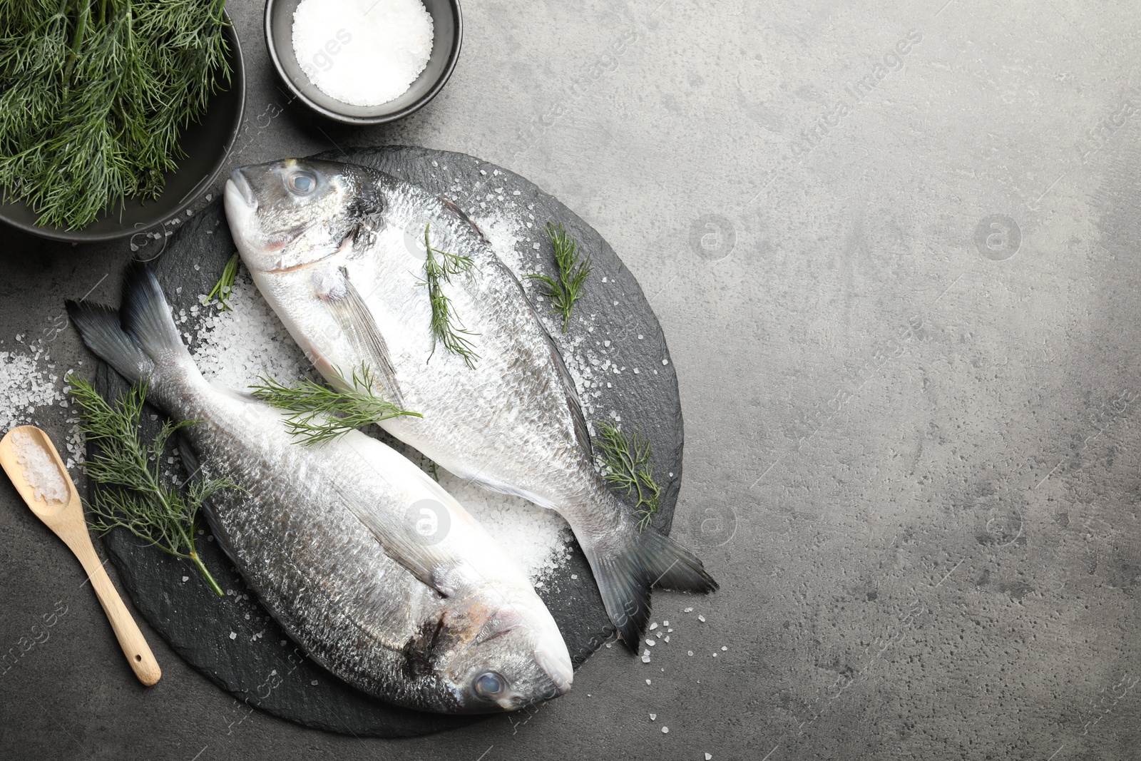 Organic seafood. Fresh raw dourade fish, salt and dill on grey table, flat lay. Space for text Photo of Organic seafood. Fresh raw dourade fish, salt and dill on grey table, flat lay. Space for text