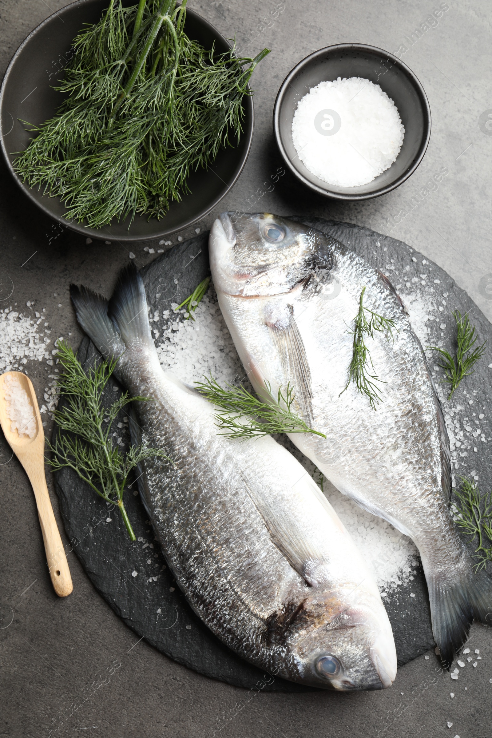 Photo of Organic seafood. Fresh raw dourade fish, salt and dill on grey table, flat lay