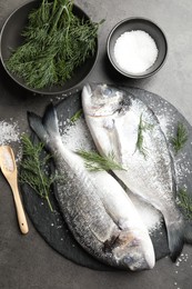 Photo of Organic seafood. Fresh raw dourade fish, salt and dill on grey table, flat lay