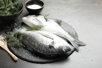 Photo of Organic seafood. Fresh raw dourade fish, salt and dill on grey table, closeup