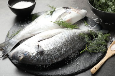Photo of Organic seafood. Fresh raw dourade fish, salt and dill on grey table, closeup