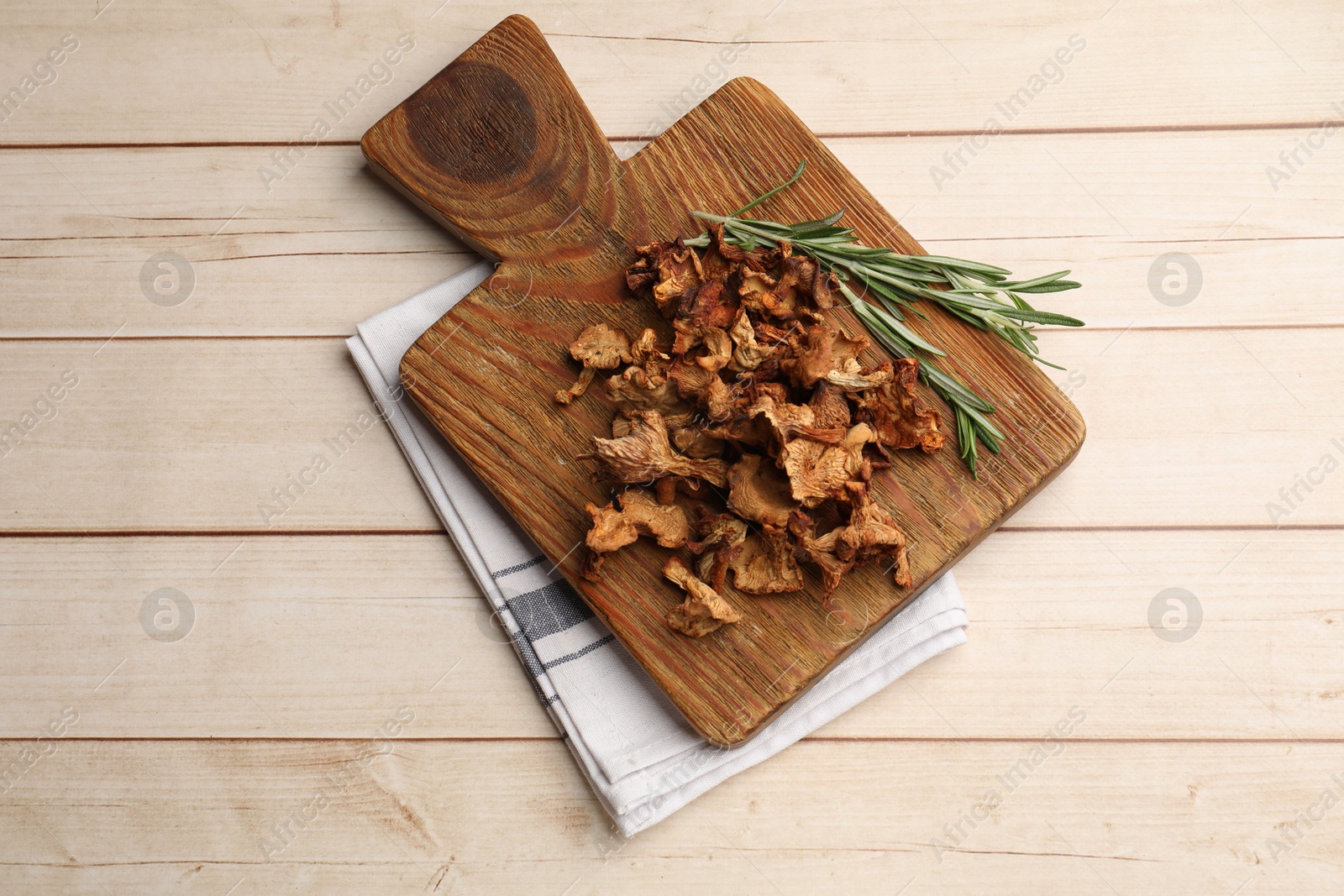 Photo of Dried chanterelle mushrooms and rosemary on light wooden table, top view