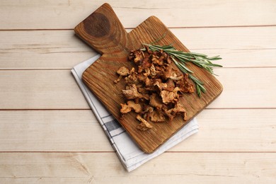 Photo of Dried chanterelle mushrooms and rosemary on light wooden table, top view