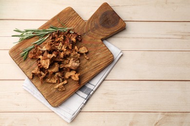 Photo of Dried chanterelle mushrooms and rosemary on light wooden table, top view. Space for text