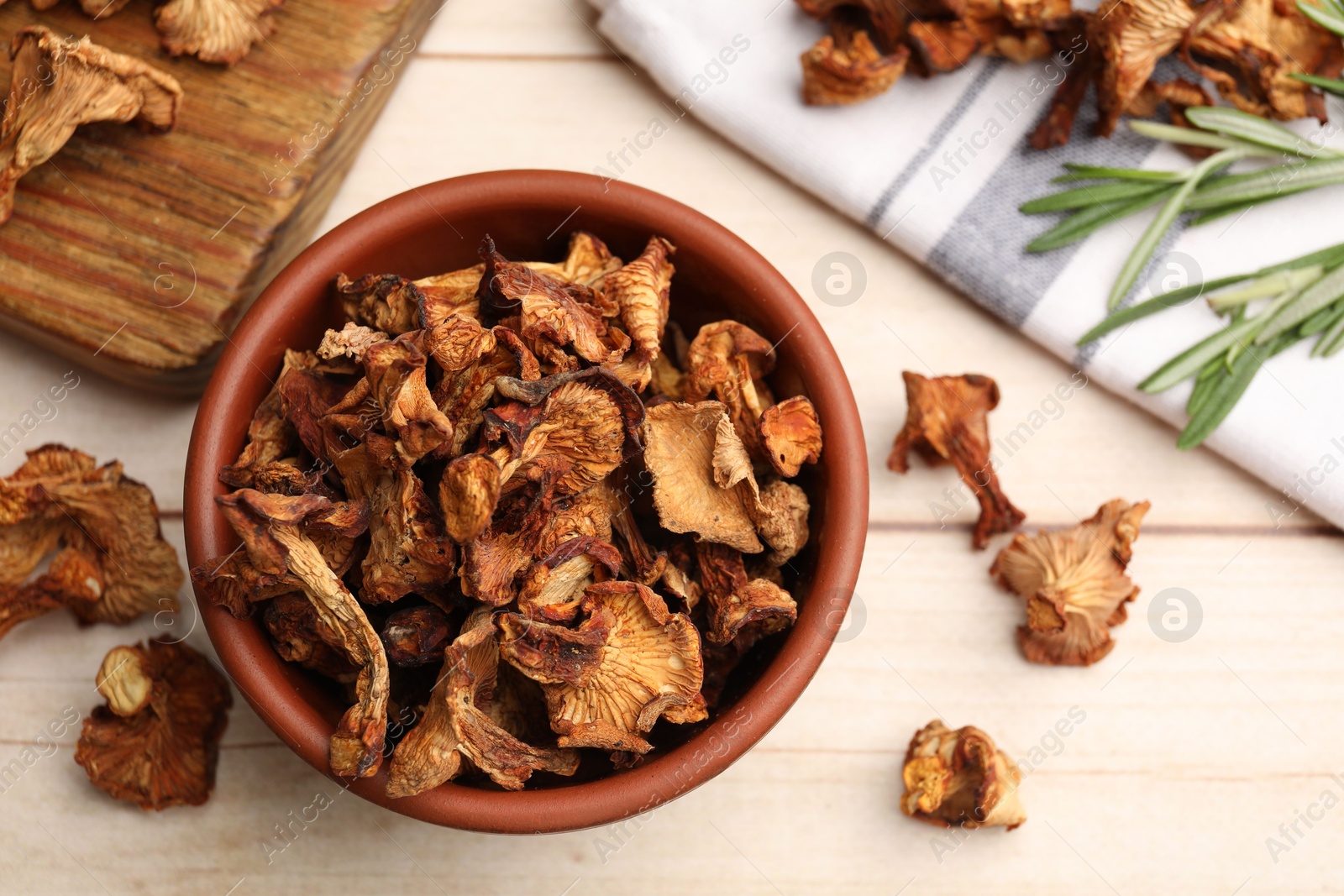 Dried chanterelle mushrooms in bowl and rosemary on light wooden table, flat lay Photo of Dried chanterelle mushrooms in bowl and rosemary on light wooden table, flat lay