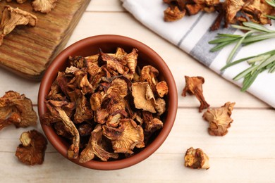Photo of Dried chanterelle mushrooms in bowl and rosemary on light wooden table, flat lay
