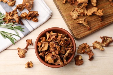 Photo of Dried chanterelle mushrooms in bowl and rosemary on light wooden table, flat lay