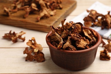 Photo of Dried chanterelle mushrooms in bowl on light wooden table, closeup