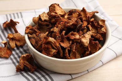 Photo of Dried chanterelle mushrooms in bowl on light wooden table, closeup