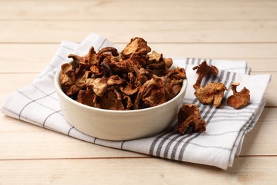 Photo of Dried chanterelle mushrooms in bowl on light wooden table, closeup