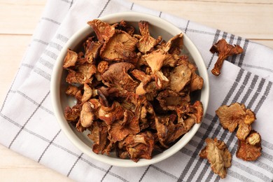 Photo of Dried chanterelle mushrooms in bowl on light wooden table, top view