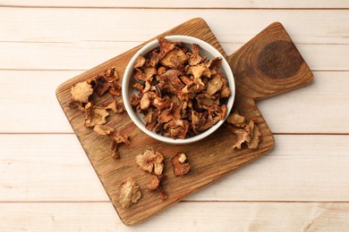Photo of Dried chanterelle mushrooms in bowl on light wooden table, top view