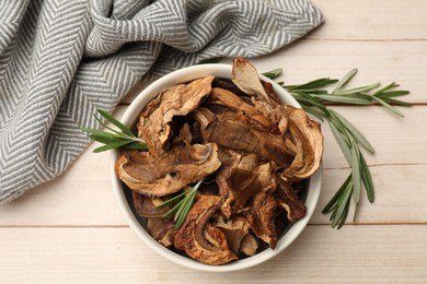 Photo of Pieces of dried mushrooms and rosemary in bowl on light wooden table, top view