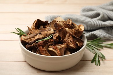 Photo of Pieces of dried mushrooms and rosemary in bowl on light wooden table, closeup