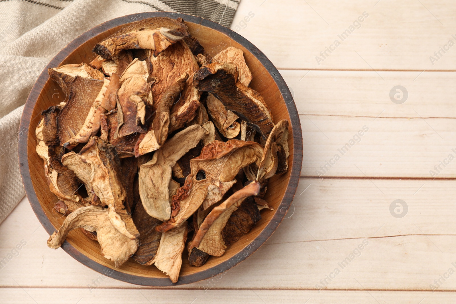 Photo of Pieces of dried mushrooms in bowl on light wooden table, top view. Space for text