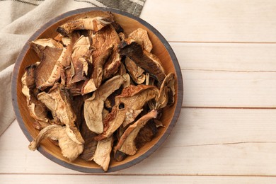 Photo of Pieces of dried mushrooms in bowl on light wooden table, top view. Space for text