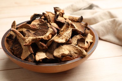 Photo of Pieces of dried mushrooms in bowl on light wooden table, closeup