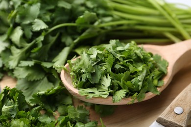 Photo of Fresh green cilantro and wooden spoon on table, closeup