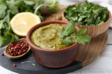 Photo of Tasty sauce with cilantro and other ingredients on white wooden table, closeup